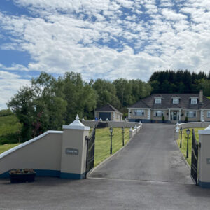 Iron gates open to a tarmac drive leading up to a large dorma bungalow