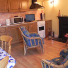 Small kitchen dining room with pine kitchen units along one wall, pine dining table and chairs and rattan chair in front of an open fire