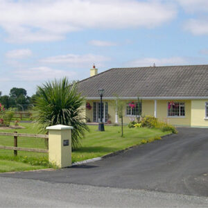 Drive leading to a yellow painted bungalow with lawn and garden to the front