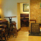 Pub with open lit fire in a brick fireplace leather seats and bar stools at round tables