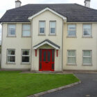 Large two storey cream painted house with grey tiled roof and entrance porch with red painted door