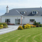 Modern dorma bungalow with a white facade, red brick accents, and a large green lawn.