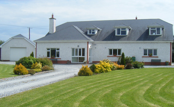 Ireland Fishing Holidays Dun Cromain Banagher (4) Modern dorma bungalow with a white facade, red brick accents, and a large green lawn.