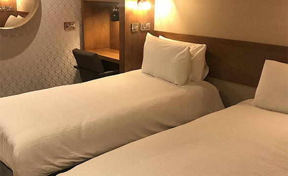A sleek twin room featuring minimalist wood accents, geometric wallpaper, and crisp white linens.