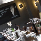 A stylish dining area with dark walls, wooden tables, and a chalkboard wall featuring a quote and illustration.