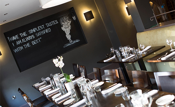 A stylish dining area with dark walls, wooden tables, and a chalkboard wall featuring a quote and illustration.