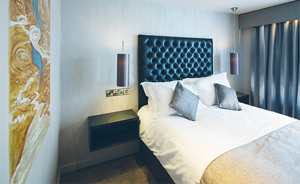 A contemporary bedroom featuring a black tufted headboard, modern pendant lighting, and an abstract yellow painting.