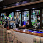 A well-stocked hotel bar with a wide selection of spirits and draught beer taps, featuring plaid-upholstered bar stools.