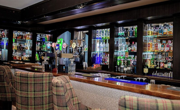 A well-stocked hotel bar with a wide selection of spirits and draught beer taps, featuring plaid-upholstered bar stools.