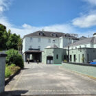 A wide-angle exterior view of the Enniskillen Hotel, showing the main entrance, "Becketts" signage, and a paved driveway under a blue sky.