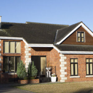 A red brick house with white corner accents, large windows, and a dark pitched roof under a clear blue sky.