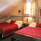 Attic bedroom with sloped ceilings featuring two beds with bright red quilted covers and a decorative purple bedside lamp.
