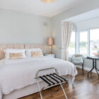 Modern bedroom with a large beige headboard, "Relax" accent pillows, and a bright bay window with a bistro seating set.