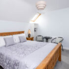 Modern attic bedroom with a large wooden bed, grey floral bedding, and a small seating area under a skylight.