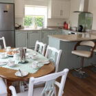 Modern sage green kitchen with granite worktops, breakfast bar, and dining table set on wood flooring.