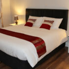 Modern double bedroom interior with red accents, black headboard, and white bedside tables.