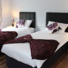 Modern twin bedroom with white bedding, purple accents, black headboards, and wood laminate flooring