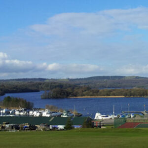 Wide landscape view of a marina filled with white cruiser boats on a large blue lake, with rolling green hills under a partly cloudy sky.