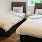 Modern twin bedroom featuring two single beds with grey tufted headboards, white linens, and blue floral accent pillows.