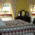 Bedroom with double bed with patterned quilt, dark wood dressing table and brown leather chair