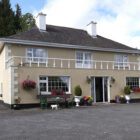 Two storey cream painted guest house with hanging baskets, flowers in pots and bench outside the front
