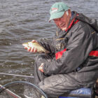 Angler sat on a wooden jetty holding a small fish