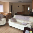 Living/dining room with two white leather settees with lilac cushions and throws, pine table and six chairs