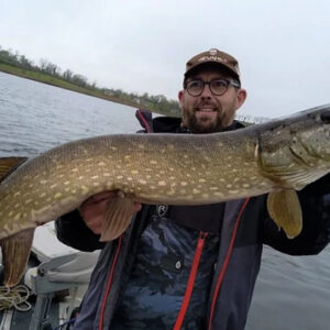 Angler holding a large pike stood on a boat on a lake