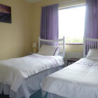 Bedroom with two single beds with white and lilac bed linen against a window with lilac curtains