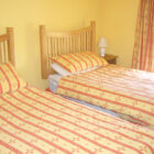 Bedroom with two single beds with pine headboard and striped yellow and orange bed linen