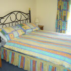 Bedroom with double bed with metal headboard and multi coloured candy striped bed linen