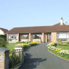 Drive way lined with daffodils leading to a stone bungalow