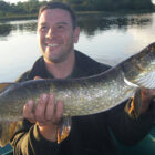 Angler sat in a boat on a lake holding a pike