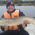 Angler sat in a boat on a lake holding a large pike