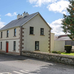 Large two storey cream painted building with red door and garden to the side with stone wall around
