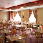 Tables set in hotel dining room with orange and white napkins in wine glasses