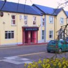 Cream painted two-storey hotel with red entrance set next to a pavement and road with a green car parked on it