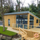 Wooden self-catering cabin with decking and steps leading to down to a river