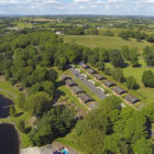 Aerial view of self-catering chalets set amongst trees next to a large lake