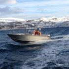 Men on an aluminium fishing boat travelling across a fjord in Norway with snow covered mountains in the background