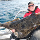 Angler on a boat holding a large halibut