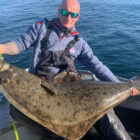 Angler on a boat holding a large halibut