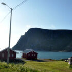 Three wood cabins on the edge of a fjord with view across the fjord to mountains