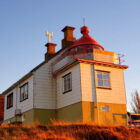 White lighthouse building with red lantern roof on a grassy hill at sunset