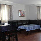 Black leather corner settee with a coffee table with blue and white checked cloth on it and black table and six chairs