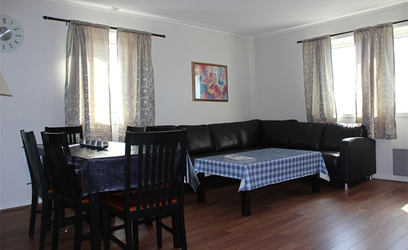 Black leather corner settee with a coffee table with blue and white checked cloth on it and black table and six chairs