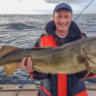 Man standing on a boat in a fjord holding a cod caught in Norway