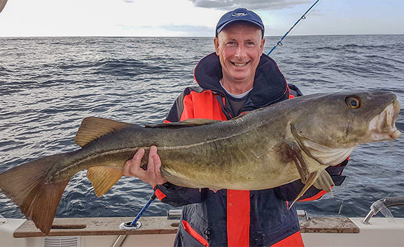 Man standing on a boat in a fjord holding a cod caught in Norway