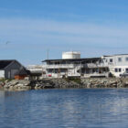 Looking across a fjord in Norway to grey two storey building with balconys