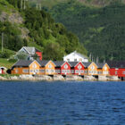 Yellow and red coloured cabins at the edge of a fjord with tree covered mountains in the background